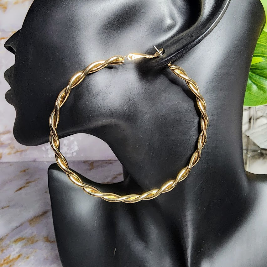 A pair of gold-colored hoop earrings displayed on a mannequin head, set against a marble background.