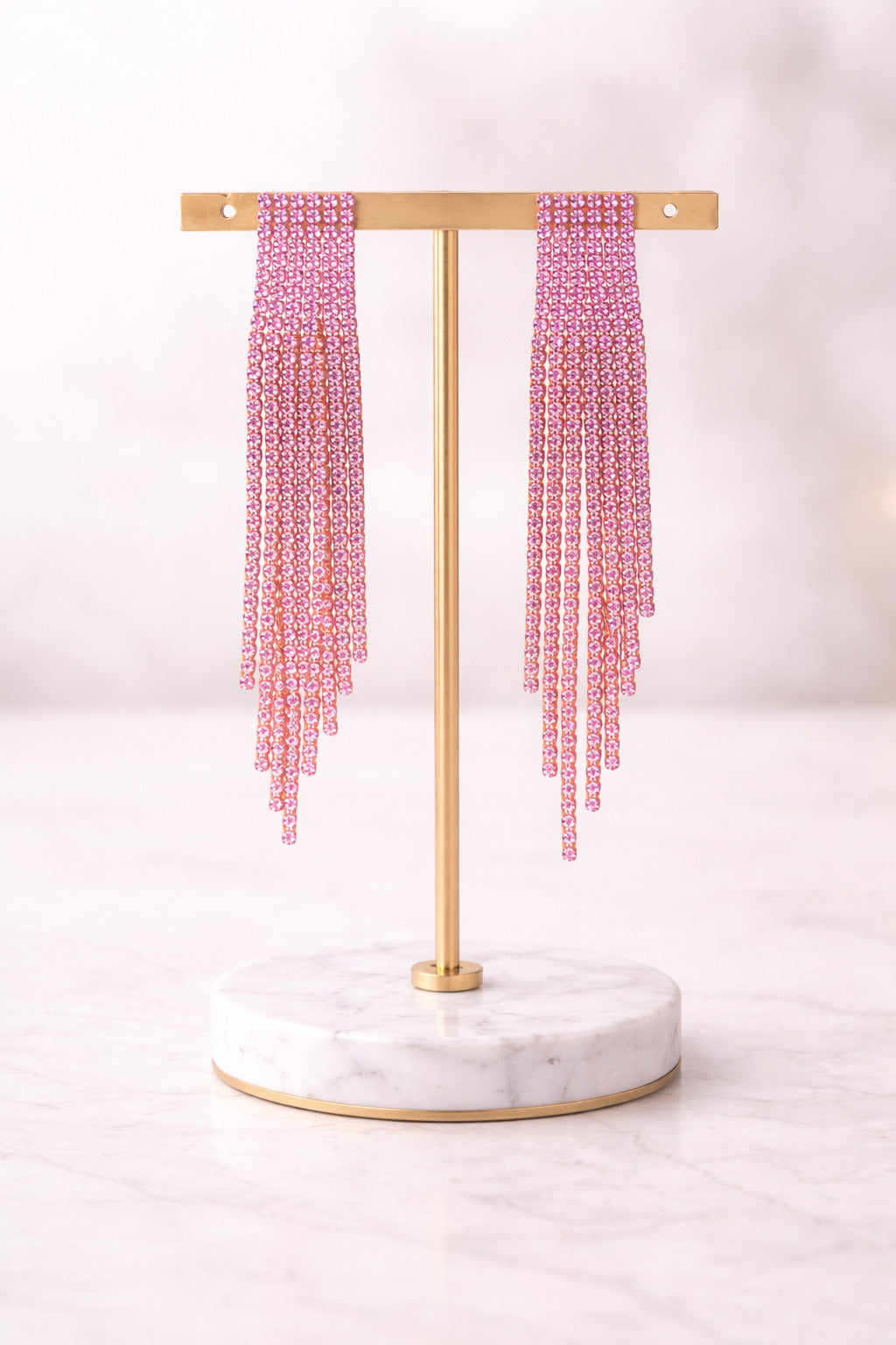 Pink beaded earrings on a gold and marble stand against a white background