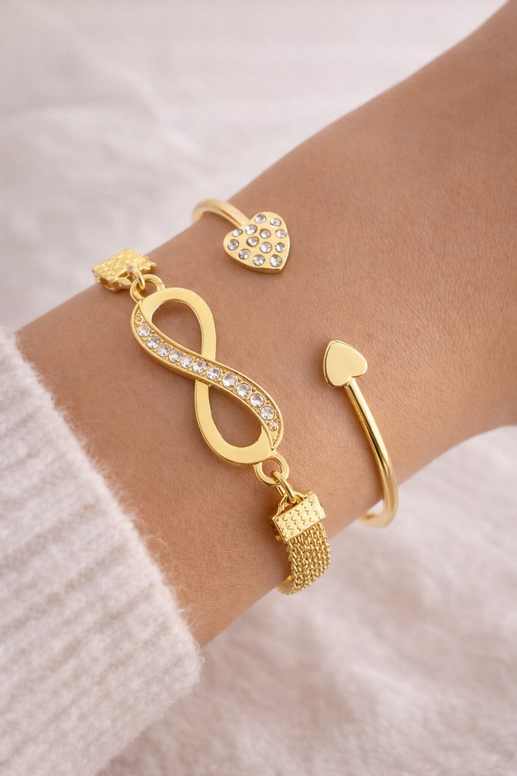 Gold bracelet with heart and infinity symbol on a wrist against a light background