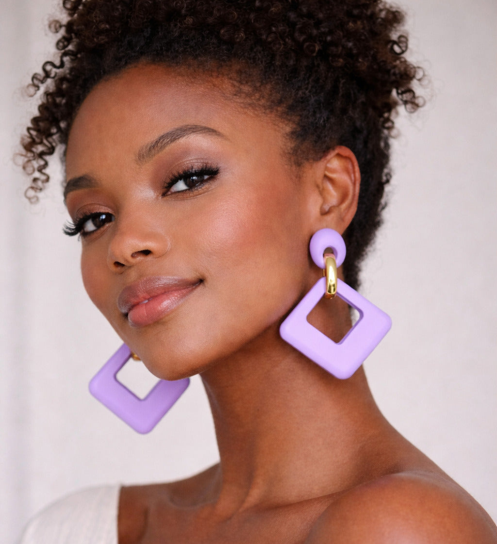 Woman wearing purple square earrings against a plain background