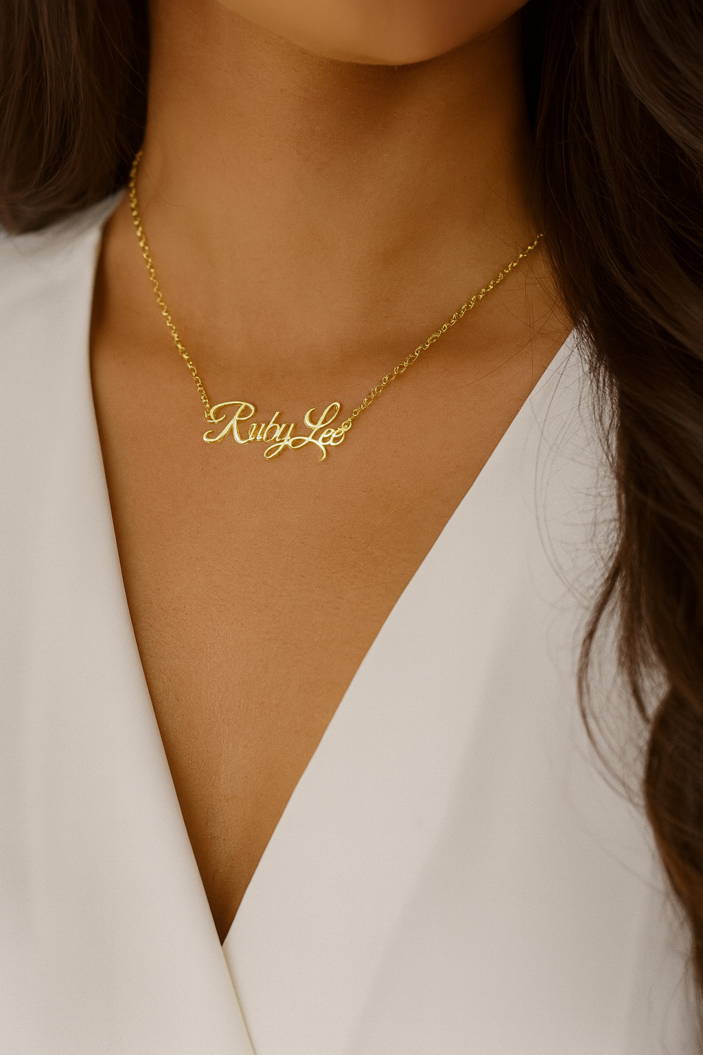 Gold necklace with 'Riley Lee' engraving worn by a person in a white outfit.