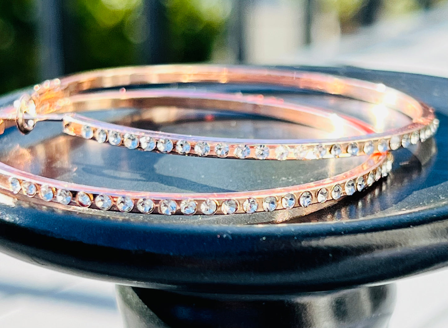 Rose gold bangles with crystal accents on a black stand outdoors