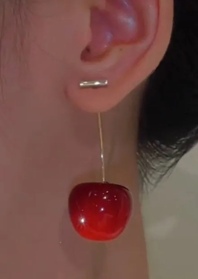 Close-up of a red cherry-shaped earring on an ear.