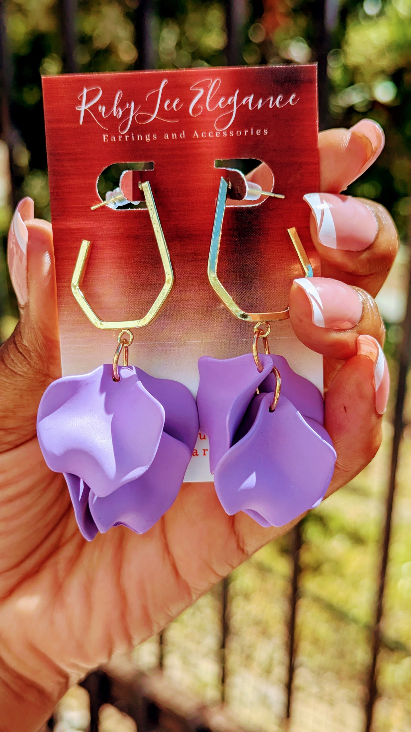 Purple flower-shaped earrings on a display card held by a hand with a blurred green background