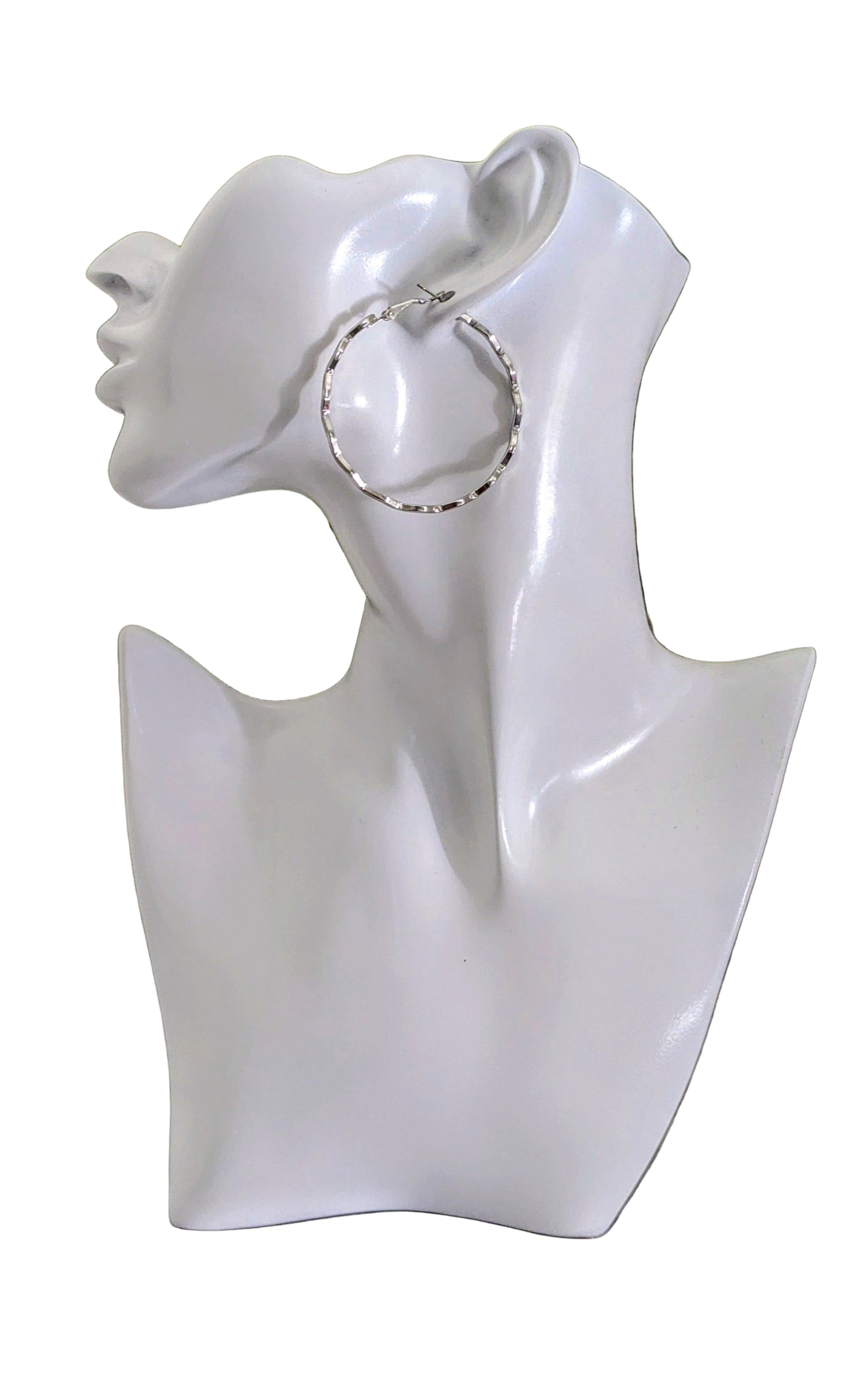 White bust with a silver hoop earring on a marble surface with greenery in the background