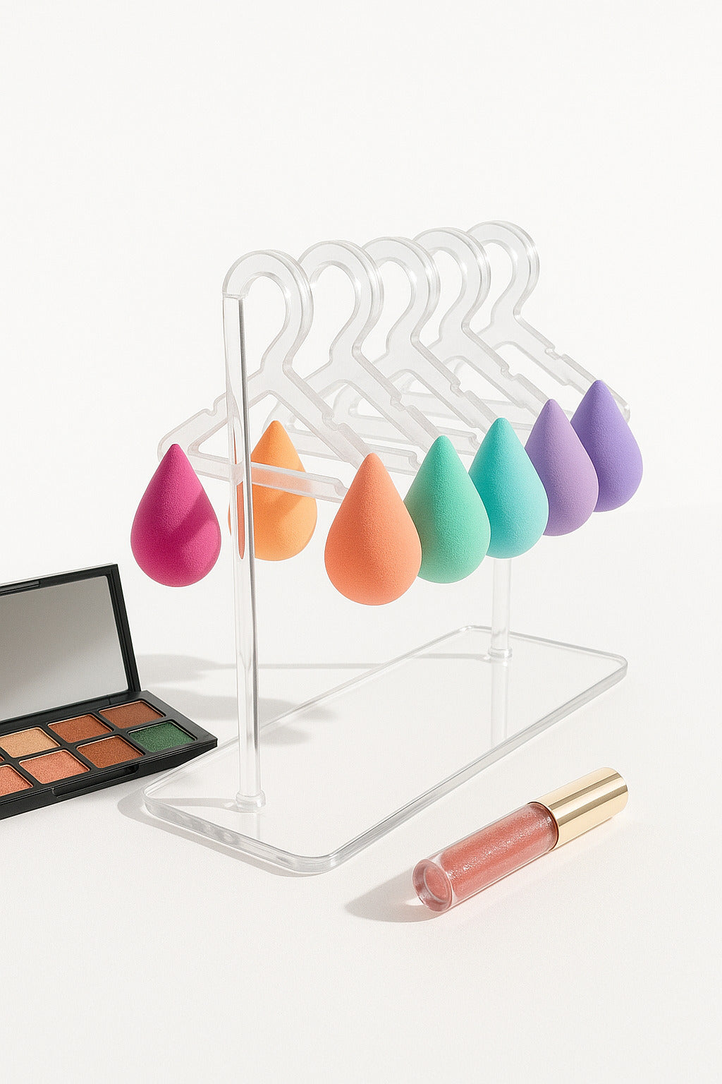 Set of colorful makeup sponges on a clear stand with a makeup palette and lip gloss.