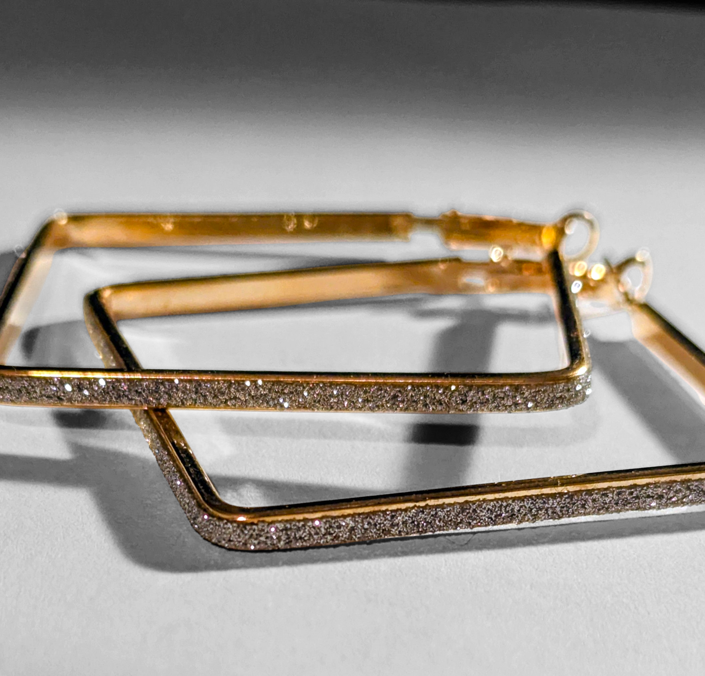 Gold hoop earrings with diamond-like stones on a light gray background