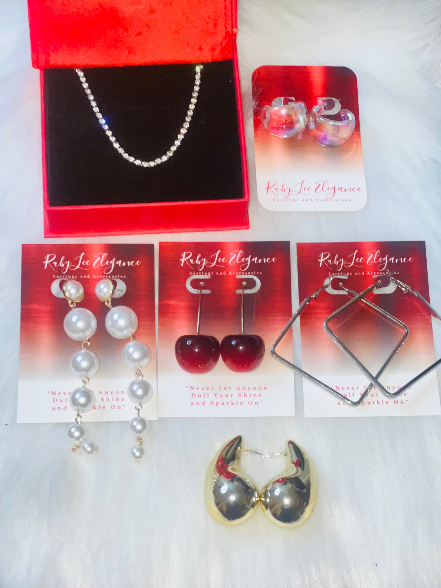 Collection of earrings on display with red and black jewelry box and cards.