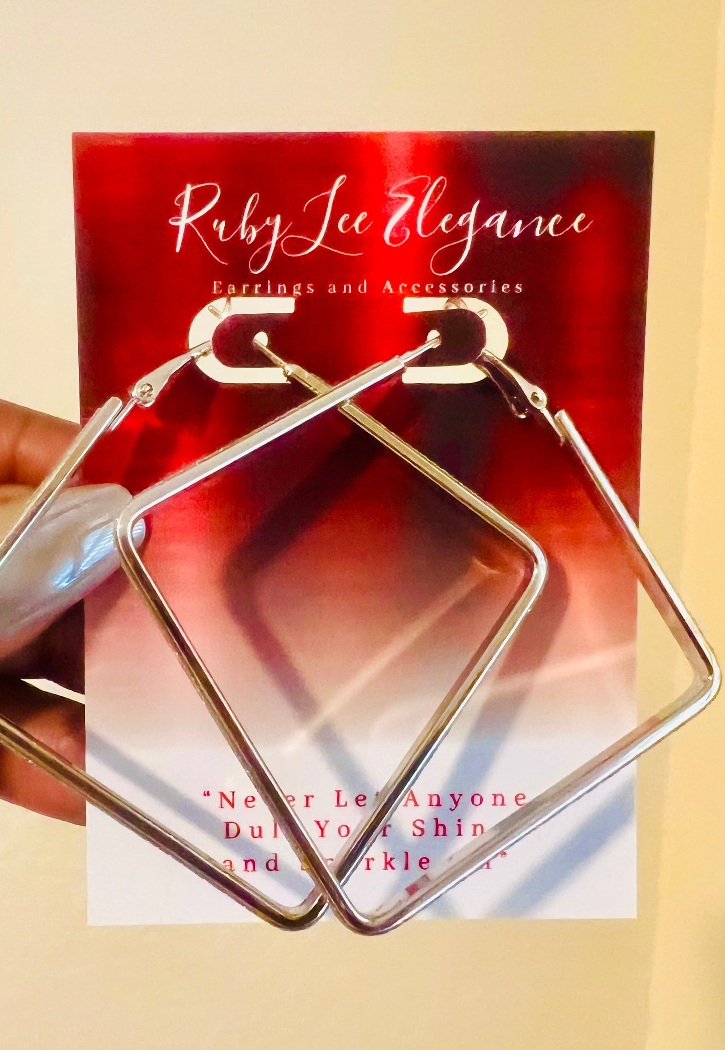 Gold square earrings held in front of a Ruby Lee Elegance card.