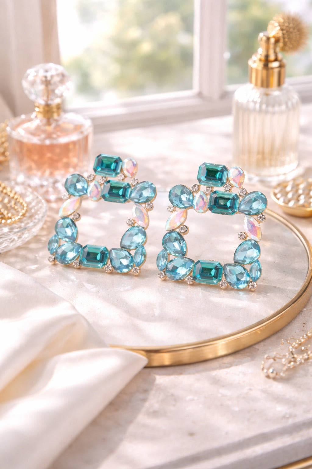 Turquoise gemstone hoop earrings on a gold stand with perfume bottles in the background.