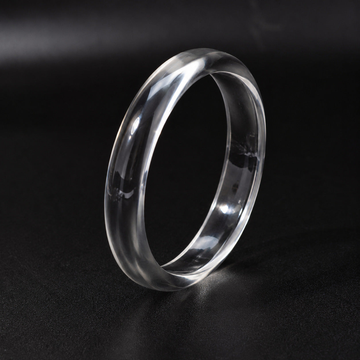 A clear, transparent bangle standing upright on a dark, reflective surface.