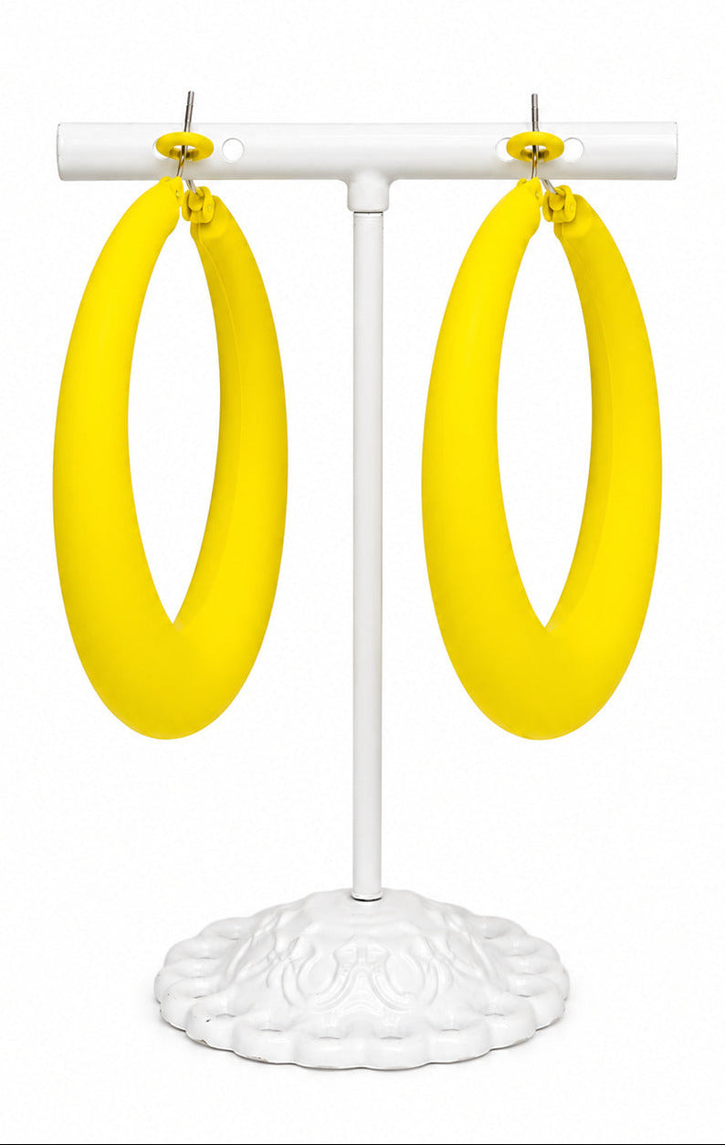 A pair of oversized bright yellow hoop earrings displayed on a white jewelry stand against a plain white background.
