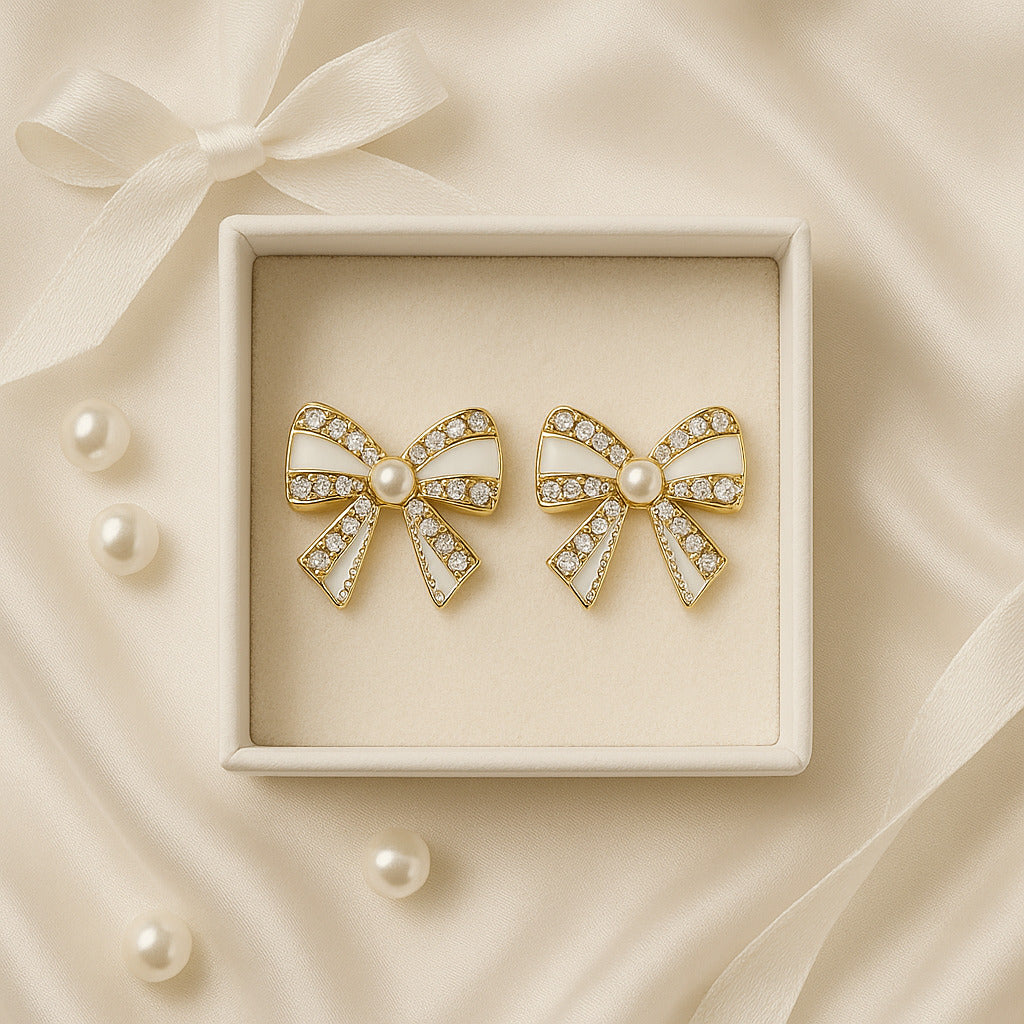 Gold bow-shaped earrings with pearls in a box on beige fabric