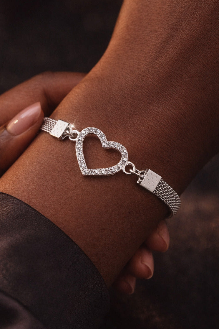 Silver bracelet with a heart charm on a wrist against a dark background