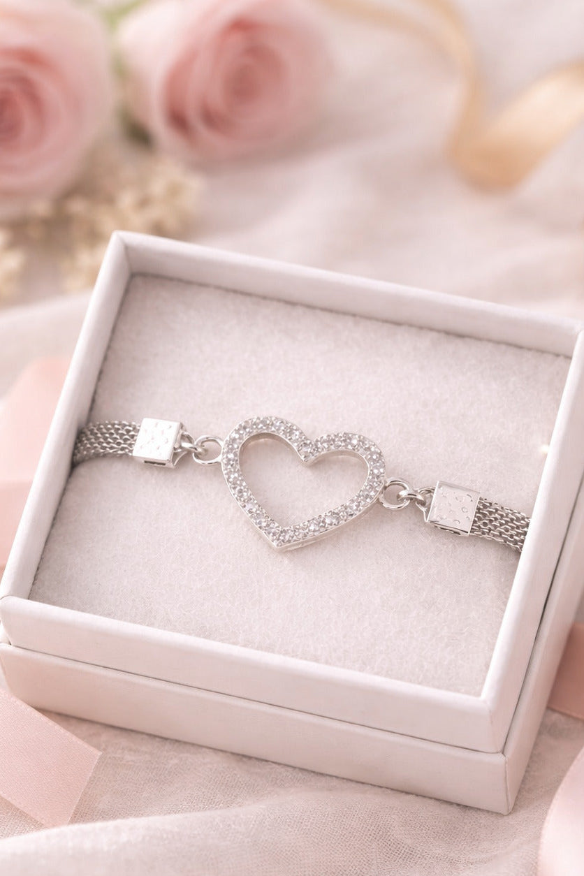 Silver bracelet with heart design in a white box on a soft pink background