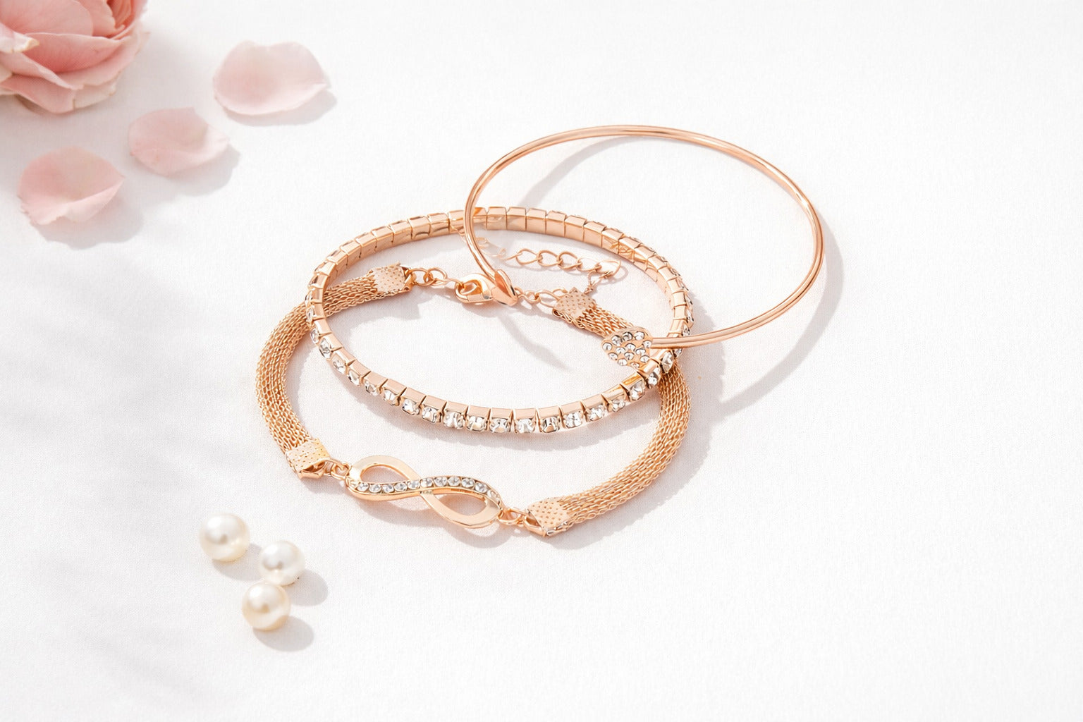 Set of rose gold bracelets on a light background with pink petals