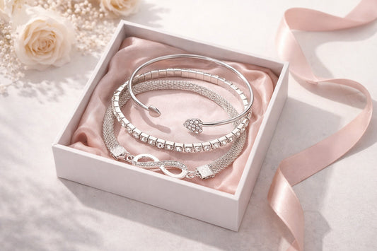 Set of silver bracelets in a white box with pink ribbon and flowers on a light background