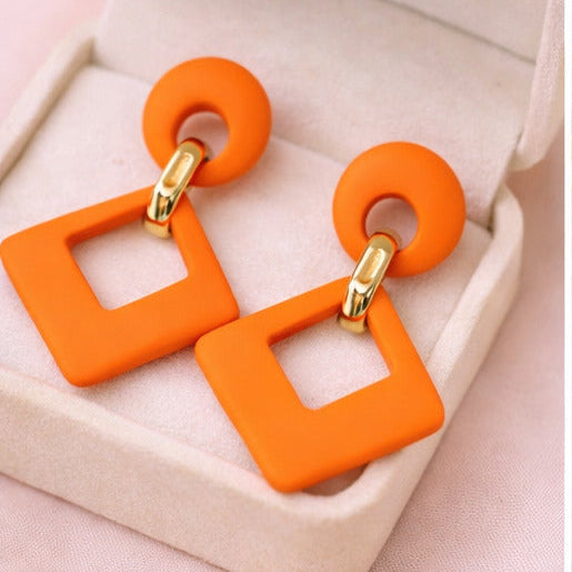 Orange square-shaped earrings with gold accents on a jewelry box and a vanity table.