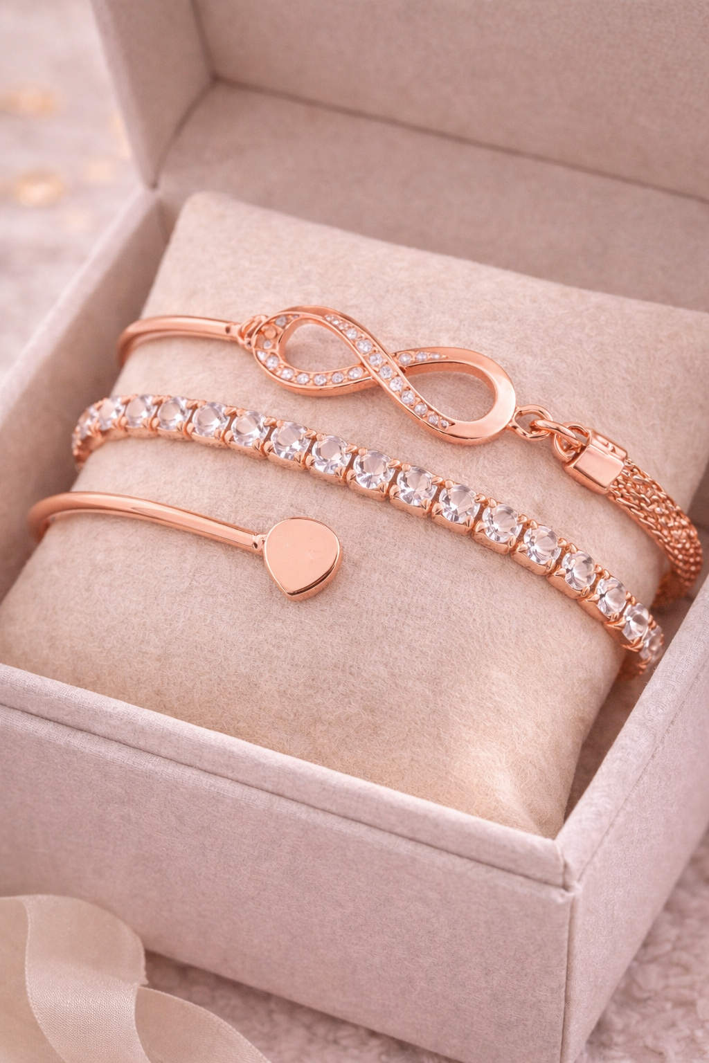 Rose gold bracelets with heart charm and infinity symbol on a soft surface