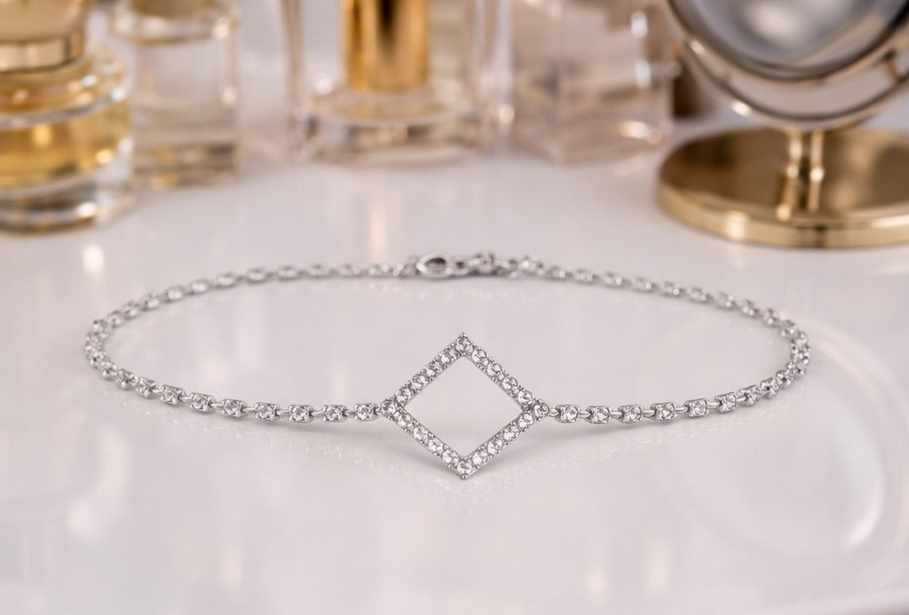 Silver bracelet on a white surface with perfume bottles in the background