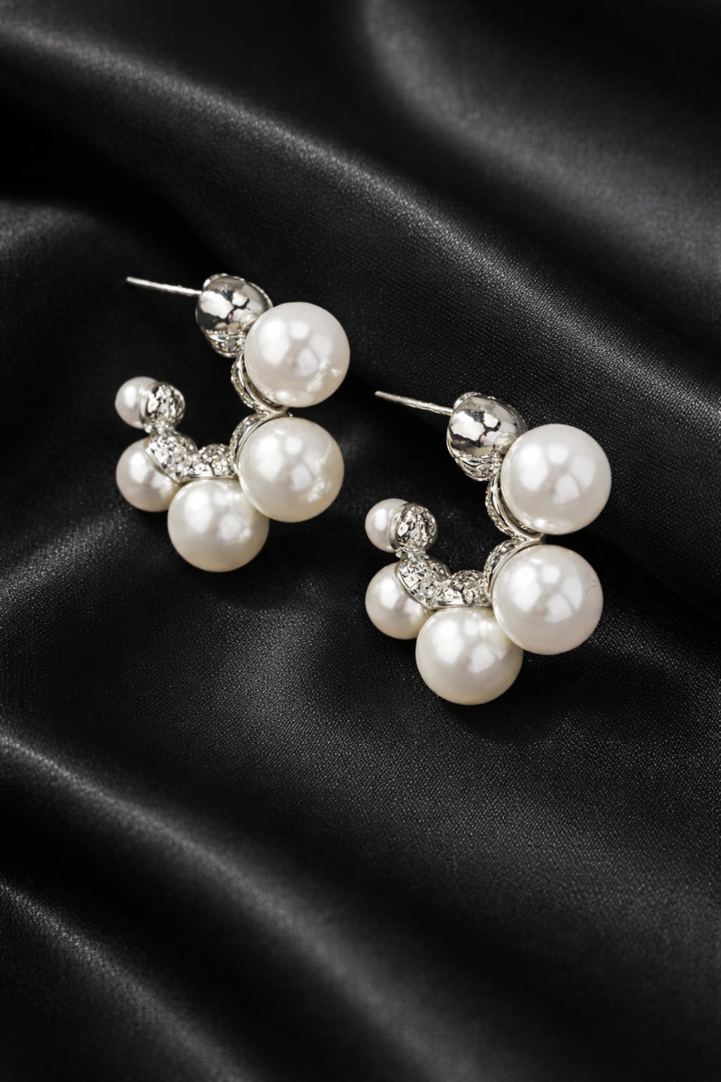 Pair of pearl and crystal earrings on a black satin background