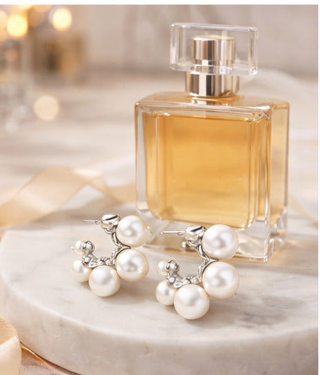 Pearl earrings displayed with perfume, jewelry, cosmetics, and flowers on a vanity table.