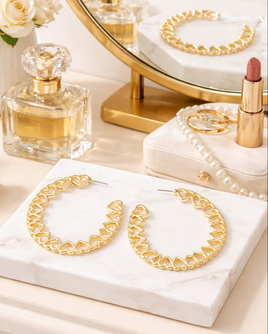 Gold hoop earrings on a marble surface with a mirror, lipstick, and perfume bottle in the background.