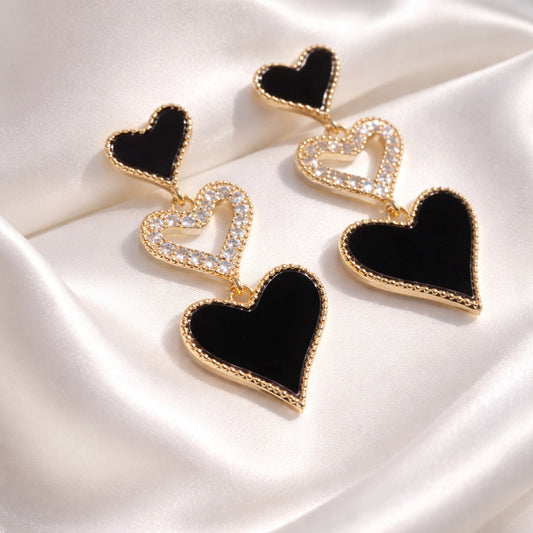 Heart-shaped earrings with black and gold details on a white satin background