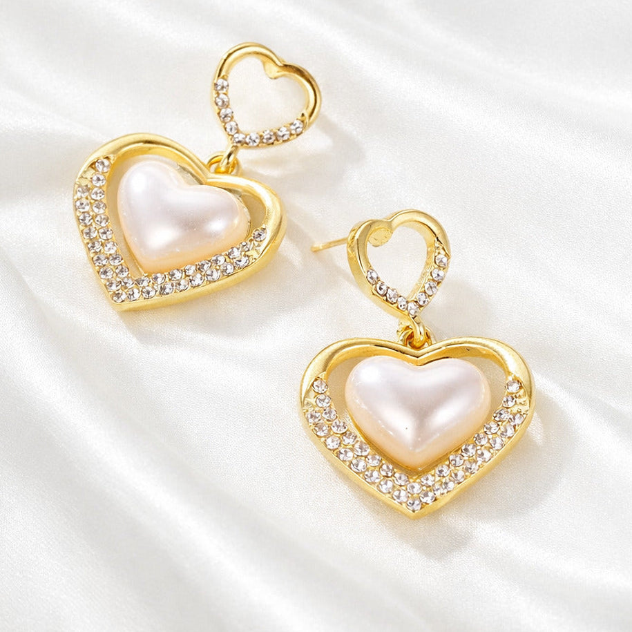 Heart-shaped earrings with gold frames and pearl centers on a white satin background