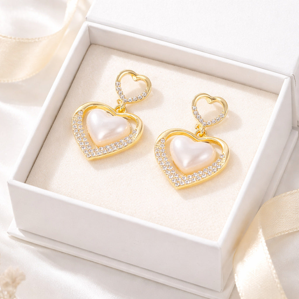 Heart-shaped earrings with pearls and gold accents in a white box.