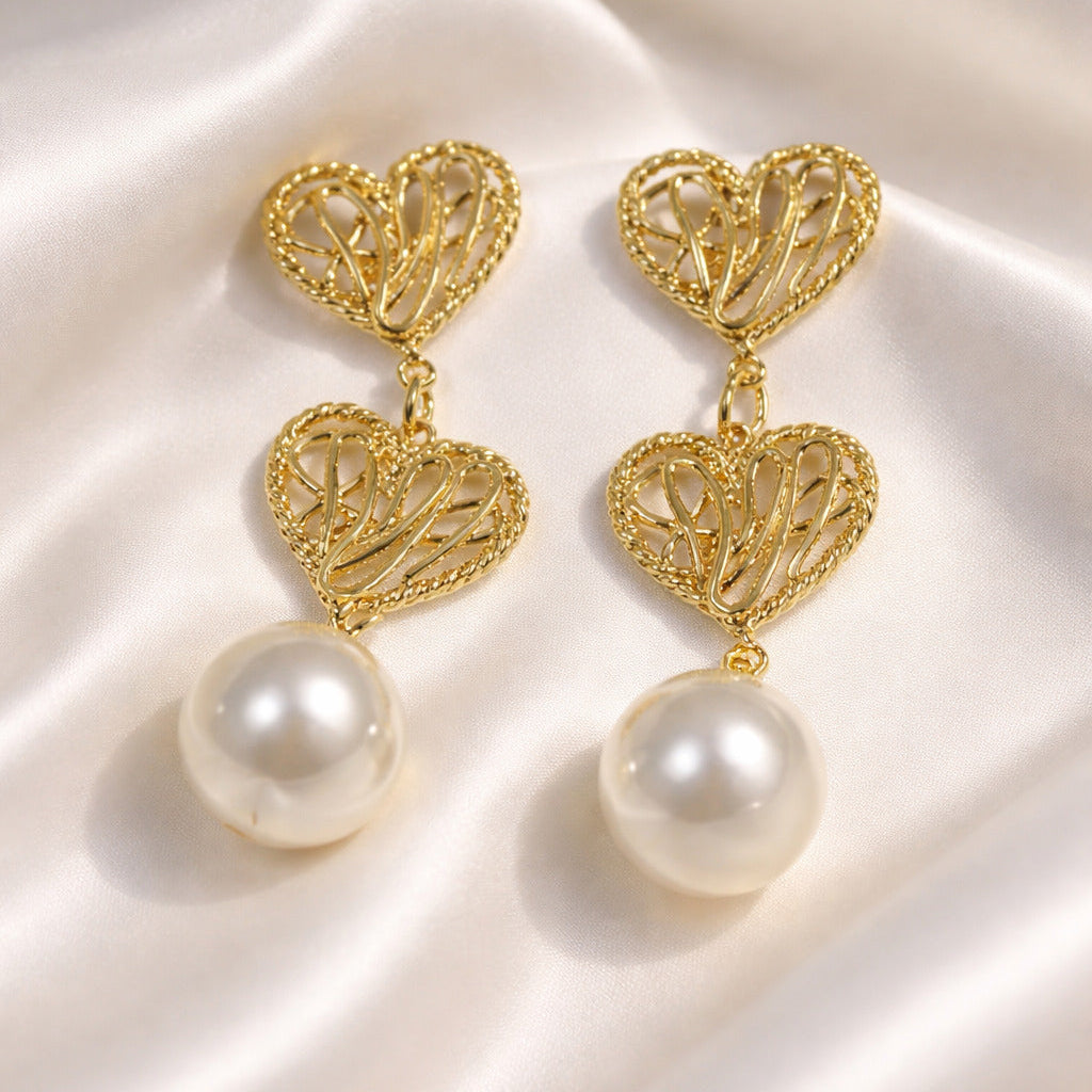 Gold heart-shaped earrings with pearl drops on a white fabric background