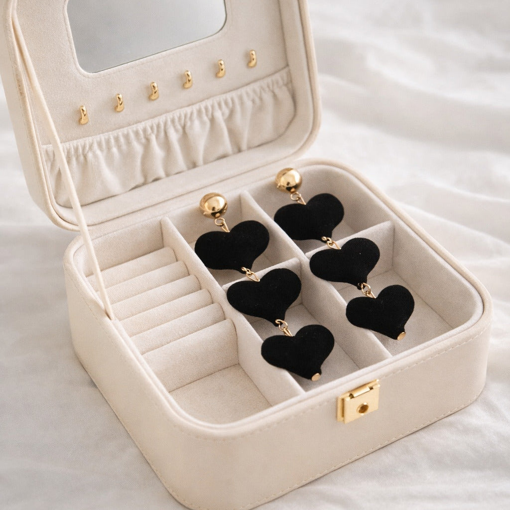 Beige jewelry box with black heart-shaped earrings on a white surface
