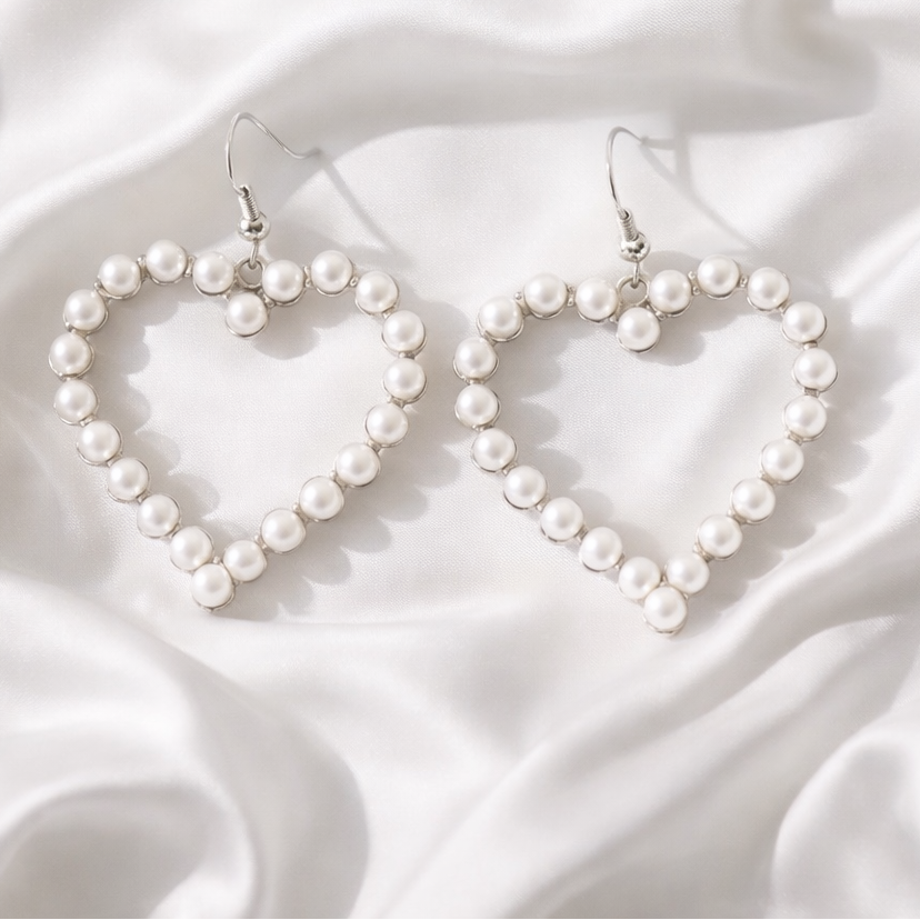 Heart-shaped pearl earrings on a white fabric background