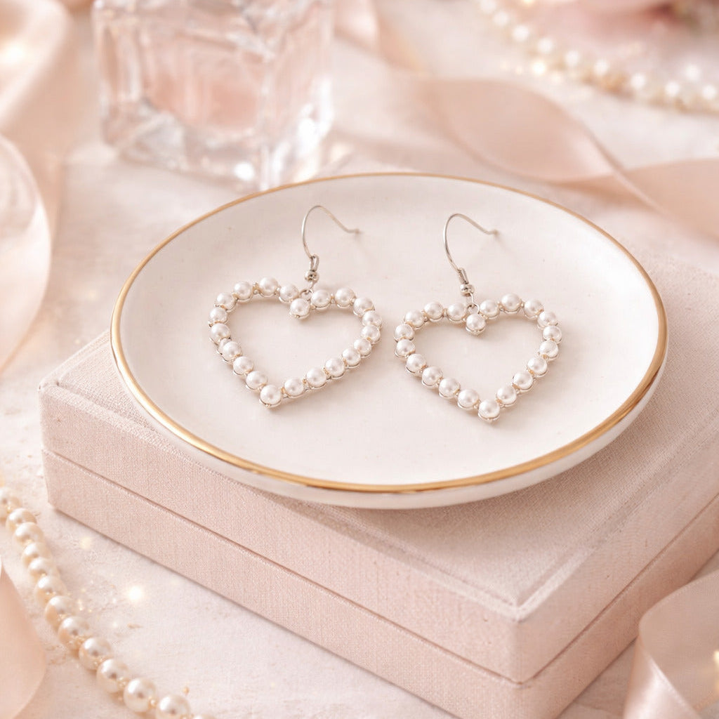 Heart-shaped pearl earrings on a white dish with a soft pink background