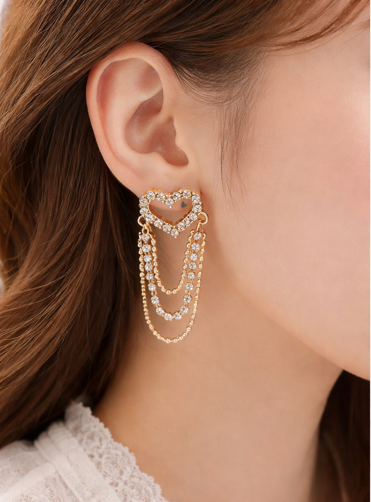 Gold heart-shaped earrings worn by a person and displayed on a marble surface.