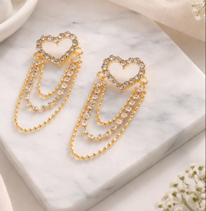 Gold heart-shaped earrings worn by a person and displayed on a marble surface.