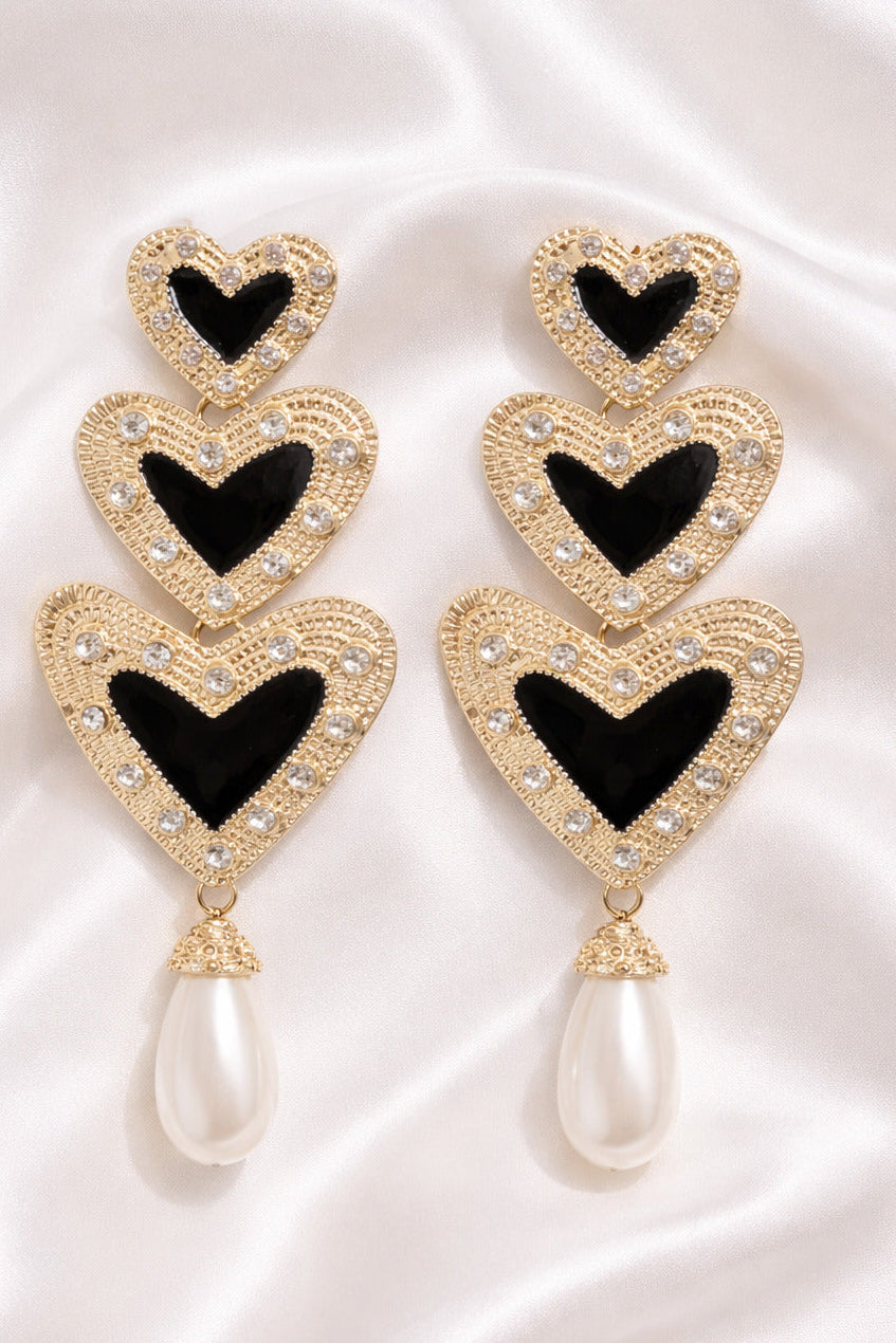 Heart-shaped earrings with black centers and gold accents on a white fabric background