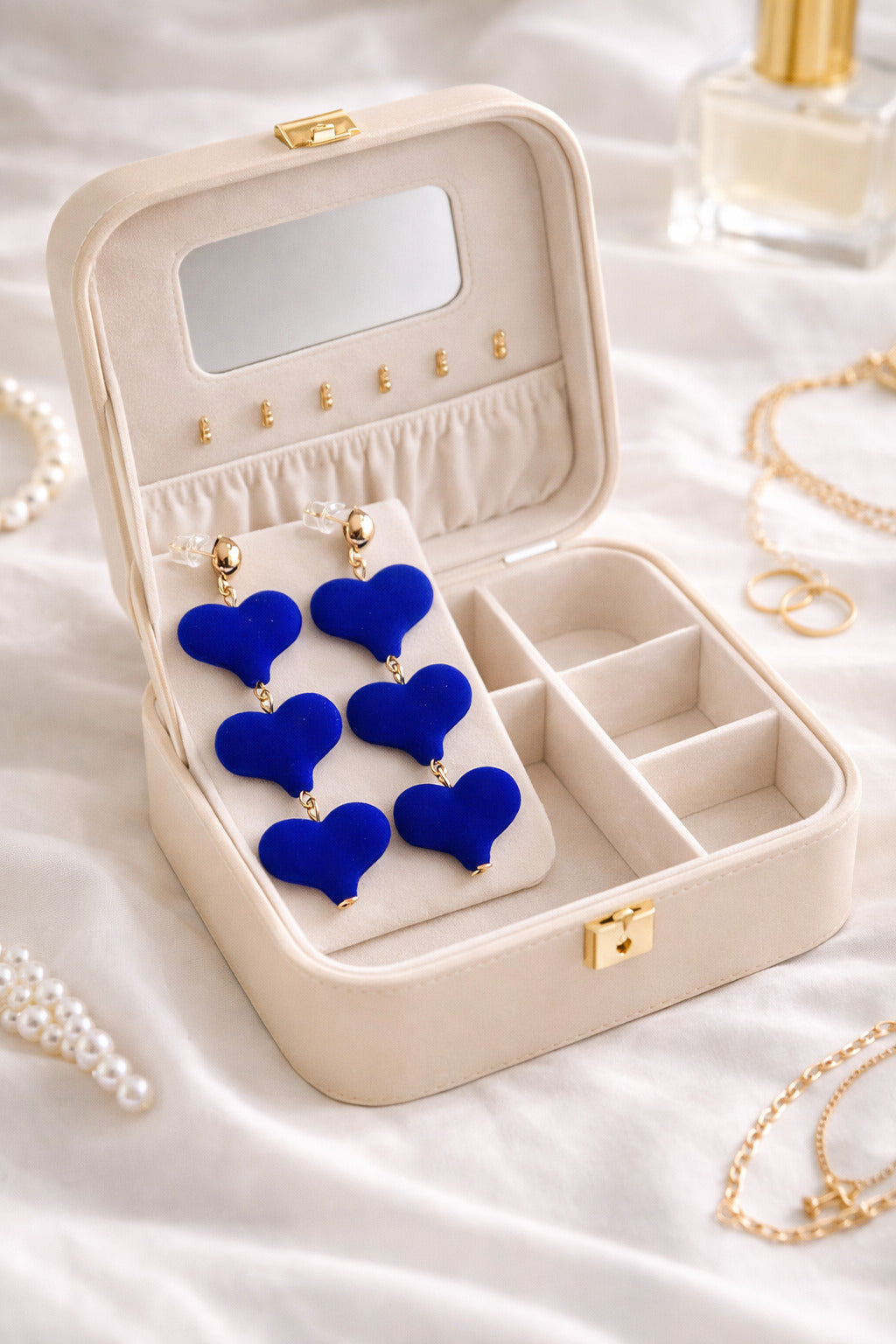 Open jewelry box with blue heart-shaped earrings on a white fabric background