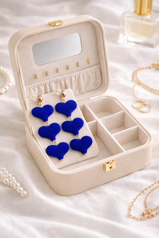 Open jewelry box with blue heart-shaped earrings on a white fabric background