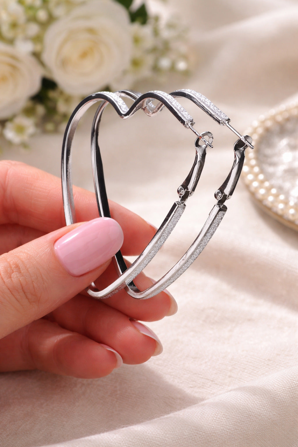 Silver heart-shaped earrings held by a hand with a soft focus background