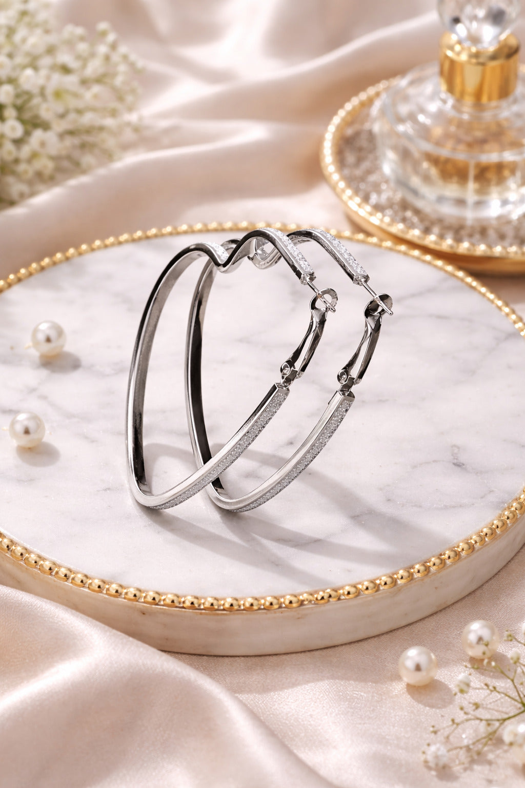 Silver hoop earrings on a marble tray with pearls and flowers