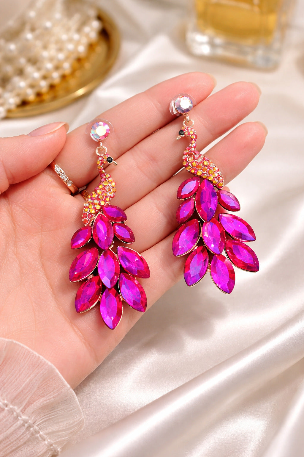 Pink earrings held in a hand with a blurred background