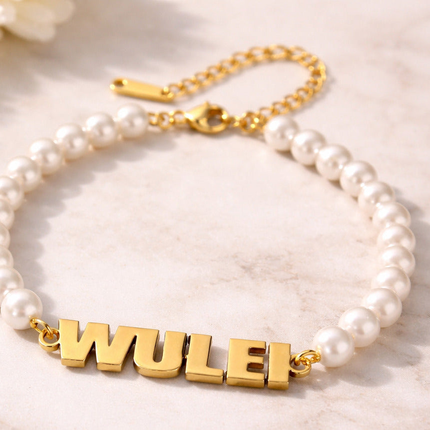 Pearl bracelet with gold 'WULEI' charm on a marble surface