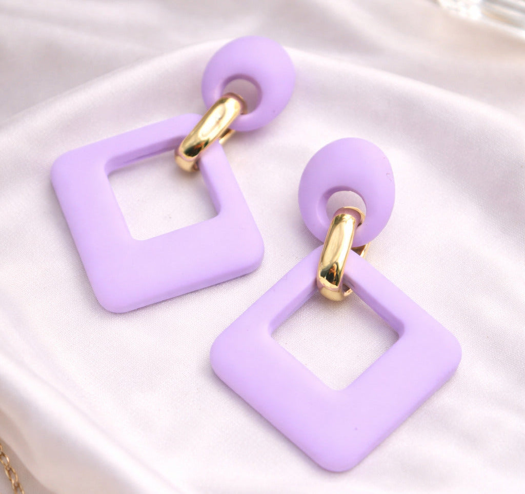 Lavender square-shaped earrings with gold accents on a white fabric background