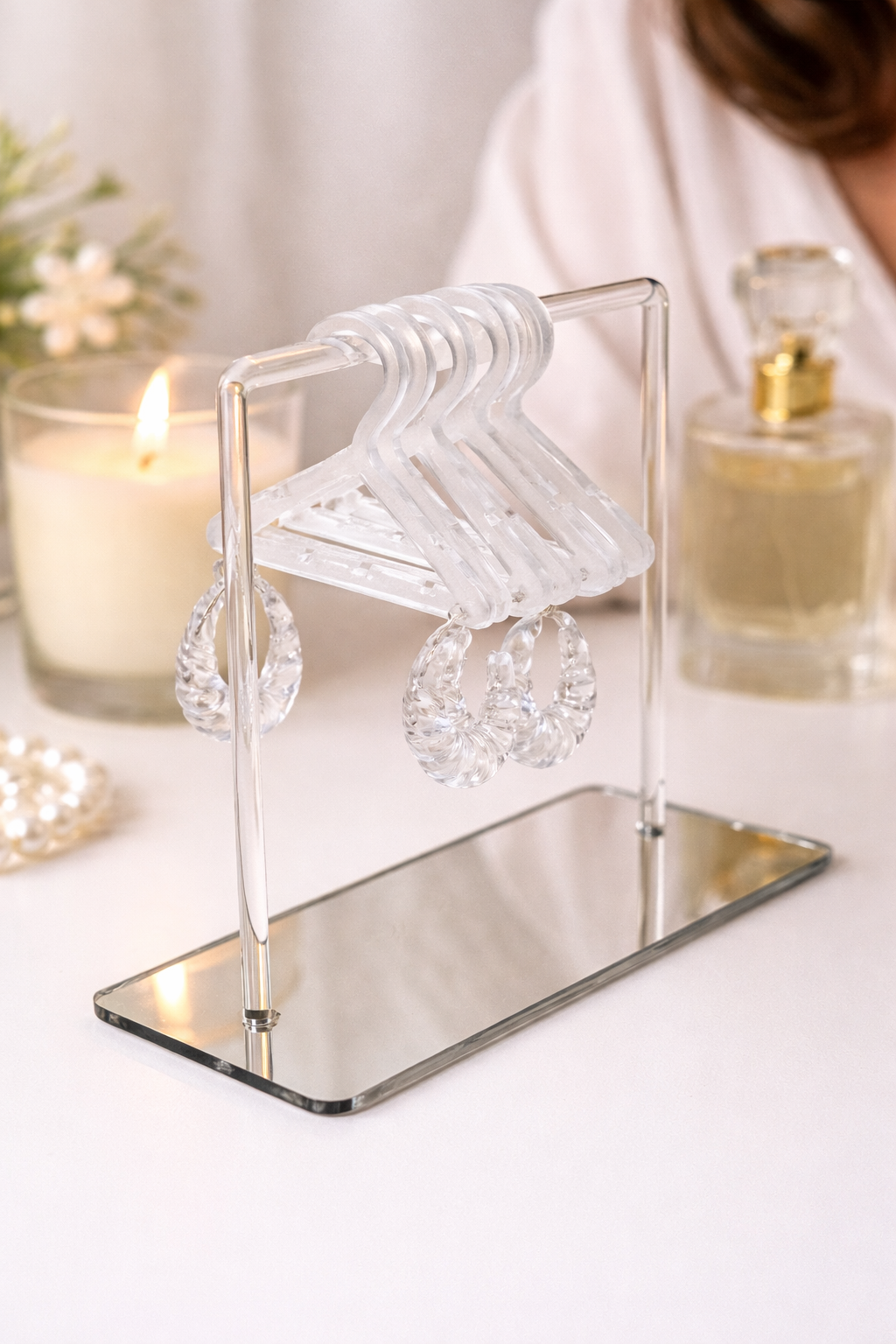 Clear crystal earrings on a mirrored stand with candles and perfume in the background
