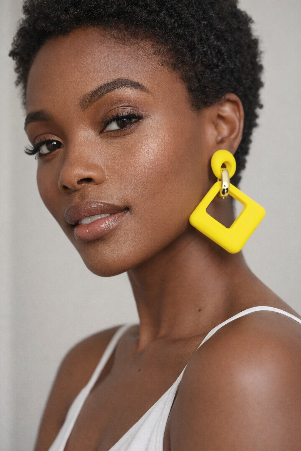 Woman wearing bright yellow square earrings against a neutral background