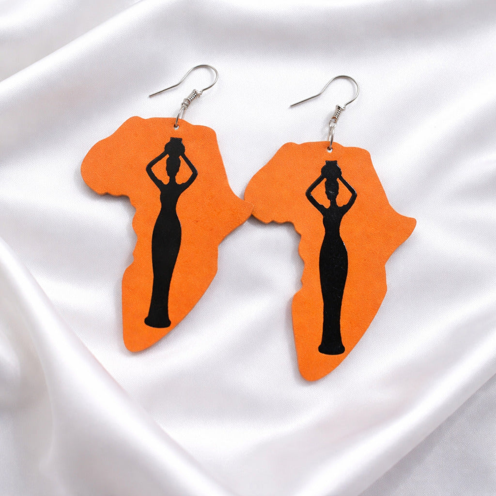 Earrings shaped like Africa with a woman silhouette on an orange background, displayed on a white fabric.