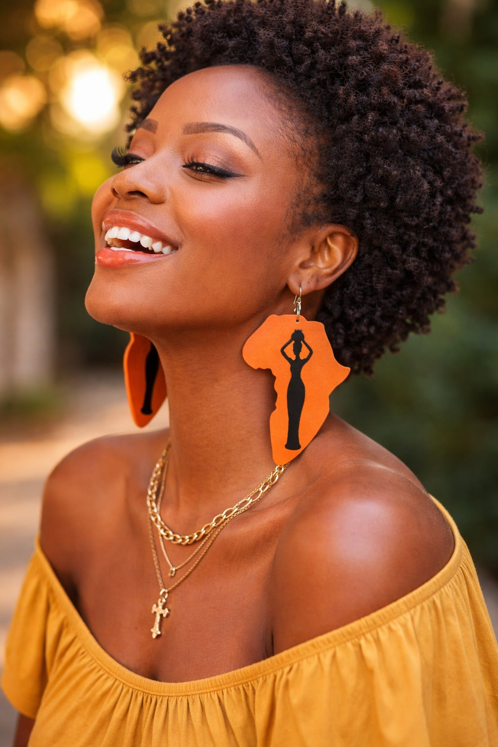 Woman wearing orange earrings with a silhouette design, smiling outdoors.