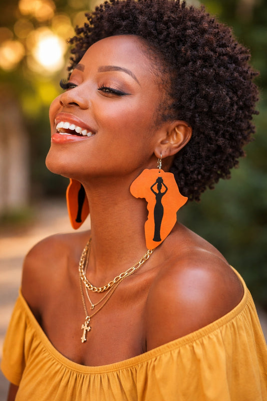 Woman wearing orange earrings with a silhouette design, smiling outdoors.