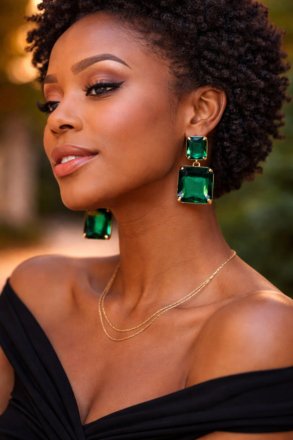 Woman wearing green earrings and a black top with a blurred background
